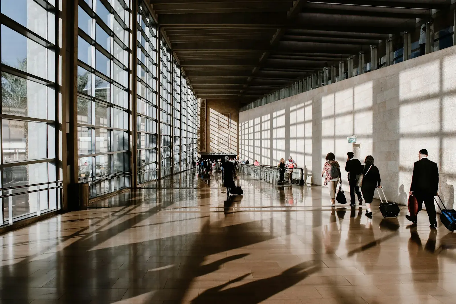 Viajeros con maletas caminando por un pasillo de aeropuerto iluminado por grandes ventanales